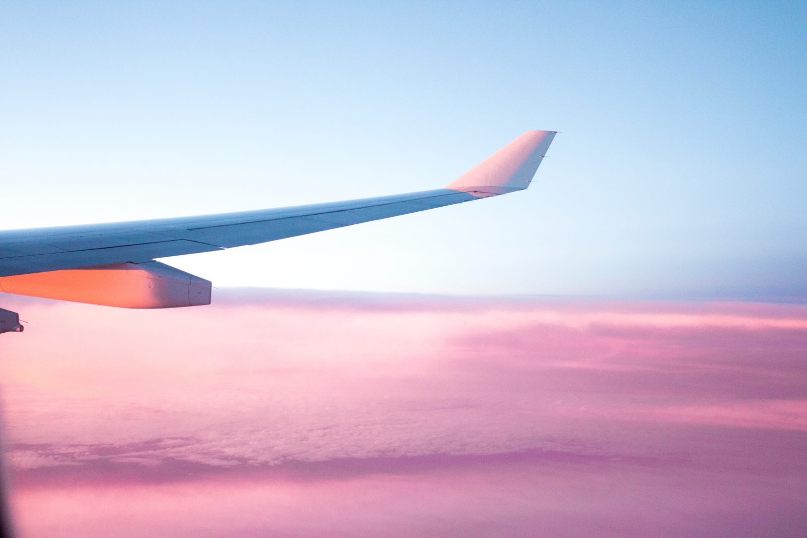 an airplane wing set against a backdrop of a beautiful blue sky and pink clouds