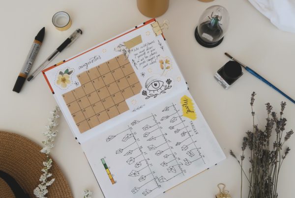 A calendar/journal surrounded by various writing implements, candles, a hat, lavender