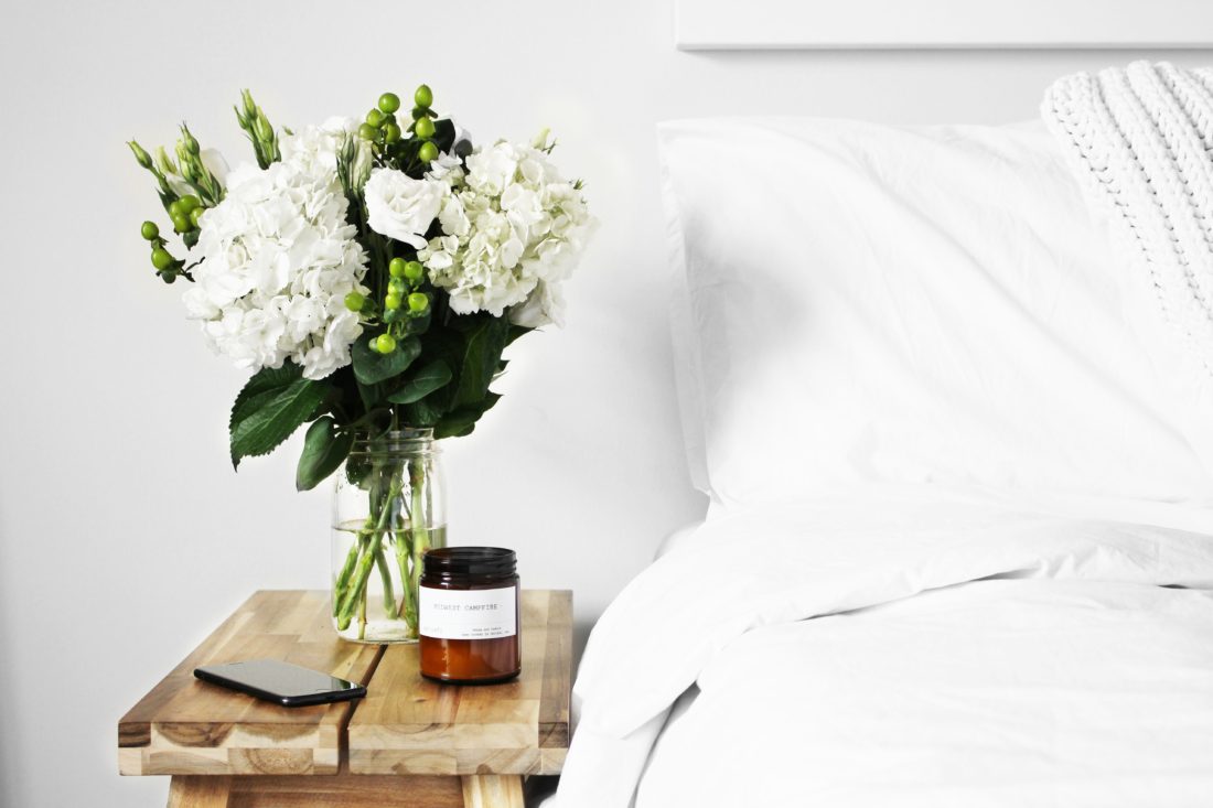 A view of a bedside table complete with a beautiful bouquet of white flowers and a candle