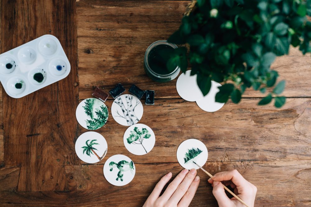 A person painting various trees on paper coasters