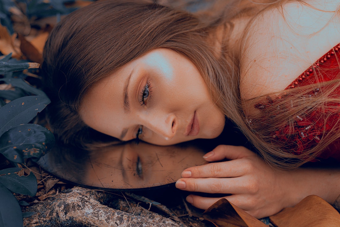 woman in red laying on the ground, her face resting on a mirror